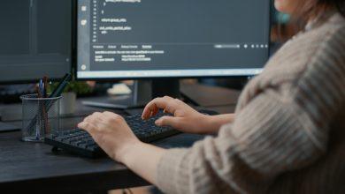 closeup caucasian software coder hands typing keyboard front computer screens with programming interface database developer sitting desk writing algorithm it agency