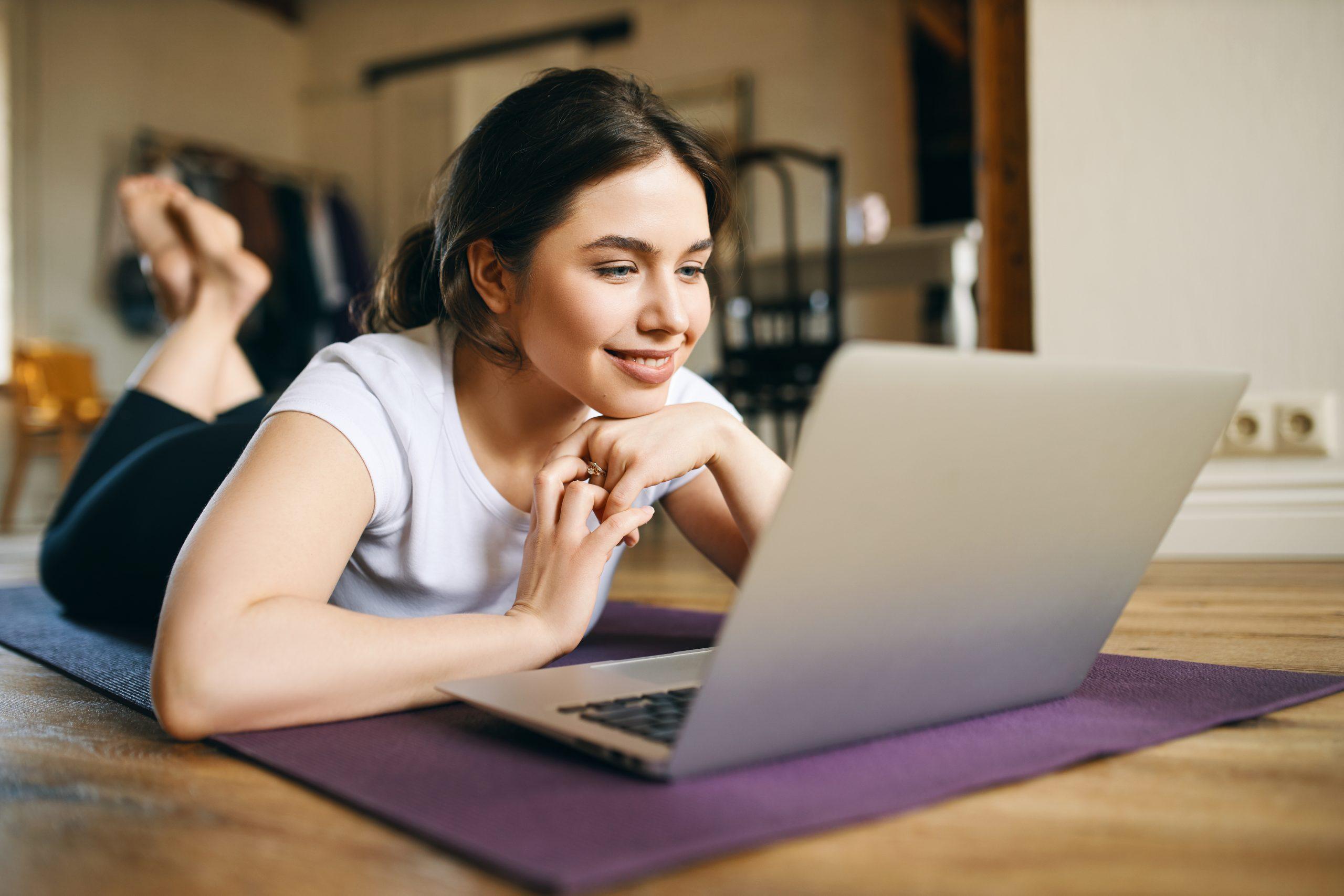 beautiful young female with muscular arms using laptop home training watching video course online has exercise indoors while social distancing having inpsired look scaled
