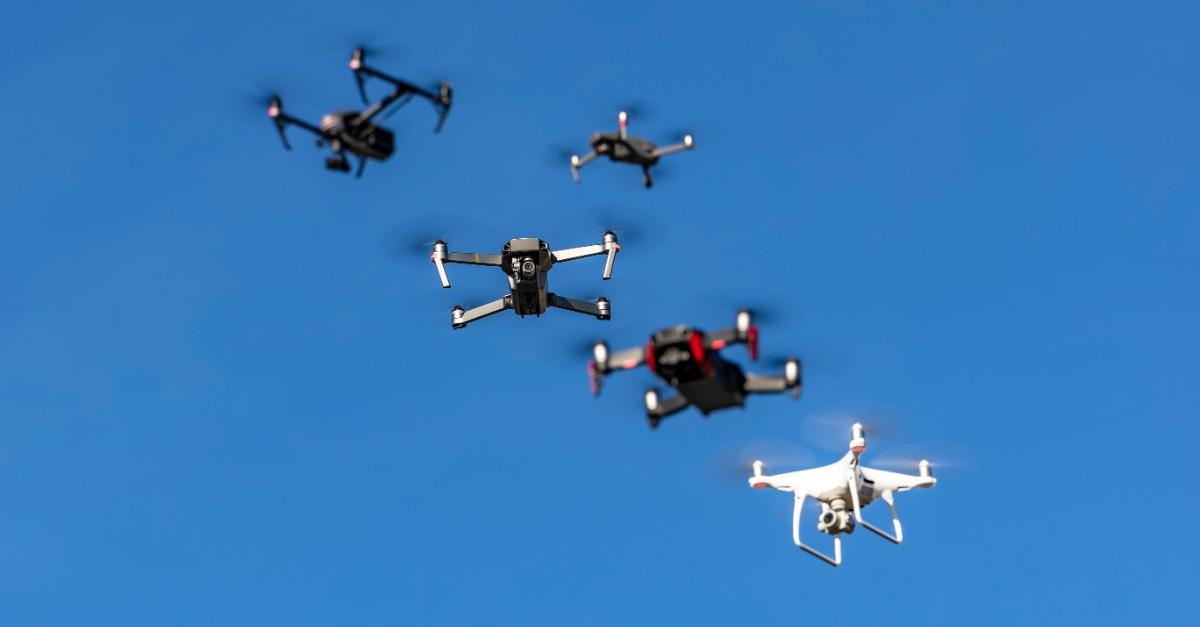 A group of drones fly through the air against a blue sky