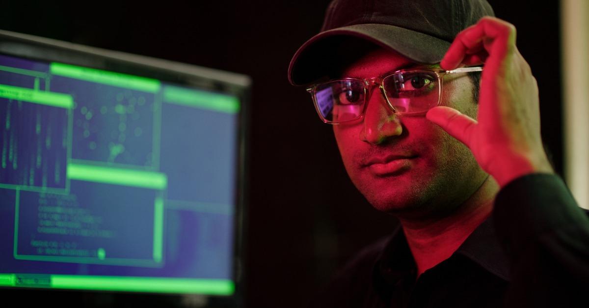 Portrait of cyber criminal adjusting glasses and looking at camera