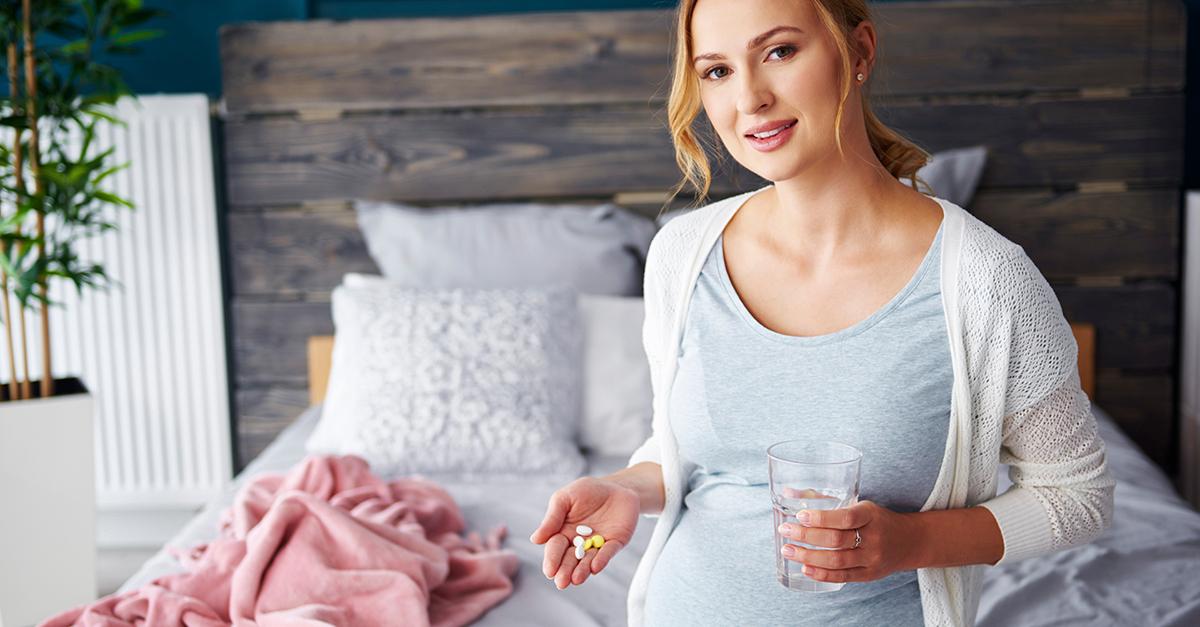 Portrait of young pregnant woman taking medicine and drinking water